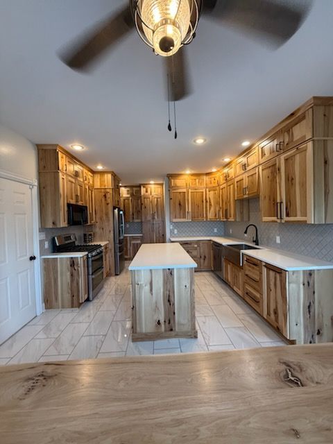 Spacious wood-paneled kitchen with island, marble tile floor, stainless appliances, and ceiling fan