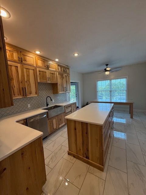 Bright kitchen with wood cabinets, white island, tiled floor, and a large window letting in daylight.