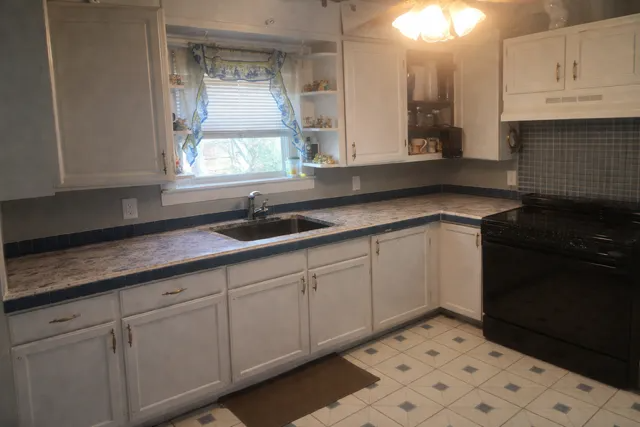 Bright kitchen with white cabinets, black countertops, sink window, and black stove.
