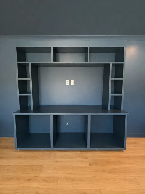 Black built-in entertainment center with shelves and cabinets against a blue wall and wood floor.