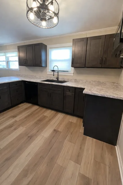 Modern kitchen with dark cabinets, light countertops, a window over the sink, and wood-look flooring