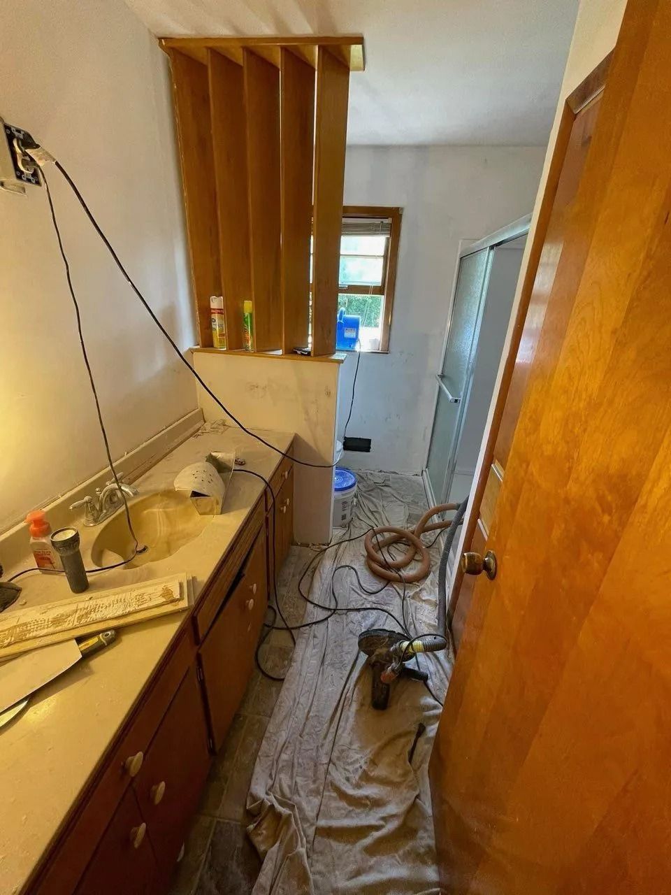 Narrow hallway under renovation with exposed wires, tools, and protective plastic covering the floor.