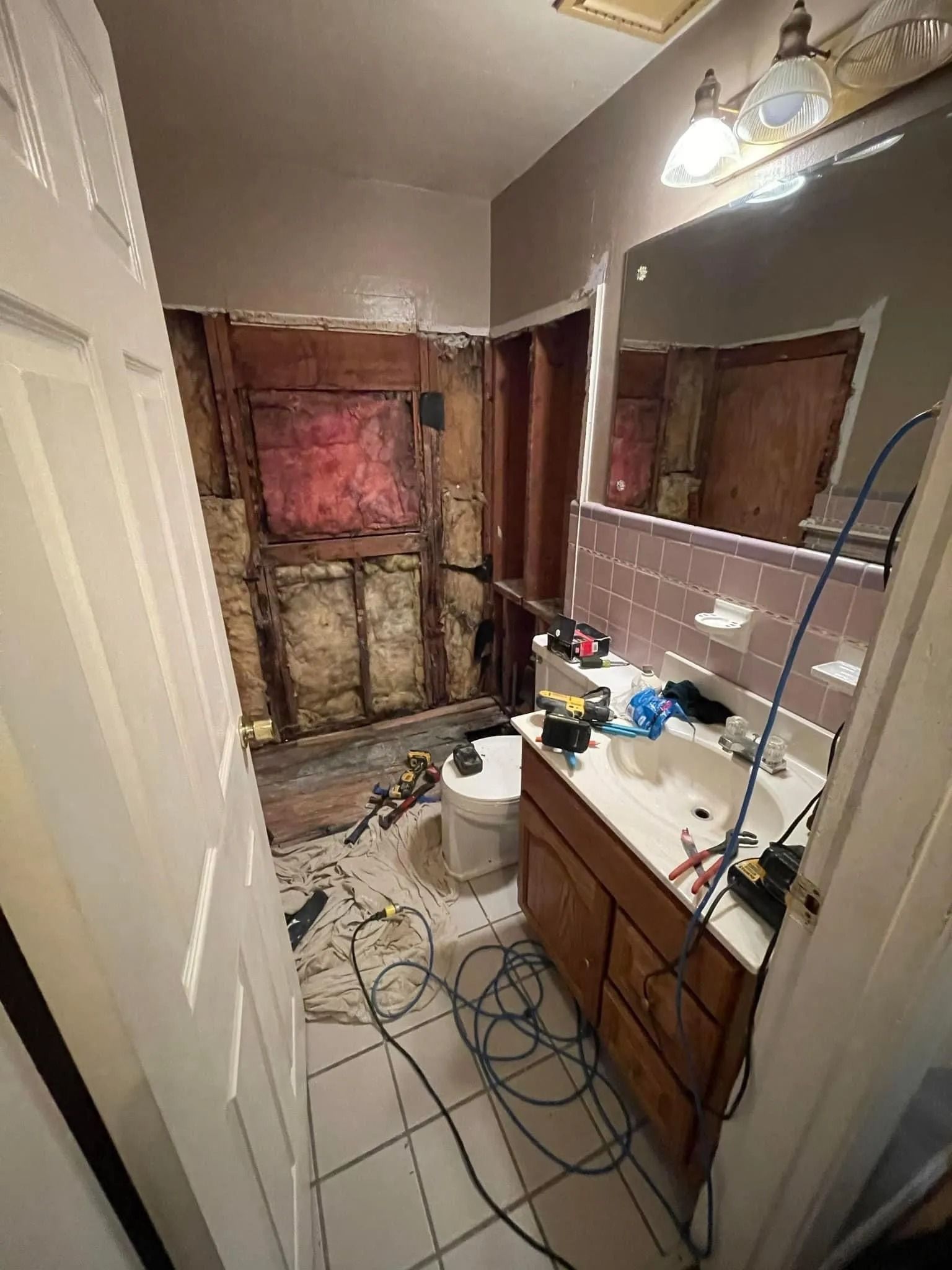 Bathroom under renovation with exposed wall studs, sink vanity, toilet, and tools on the floor.