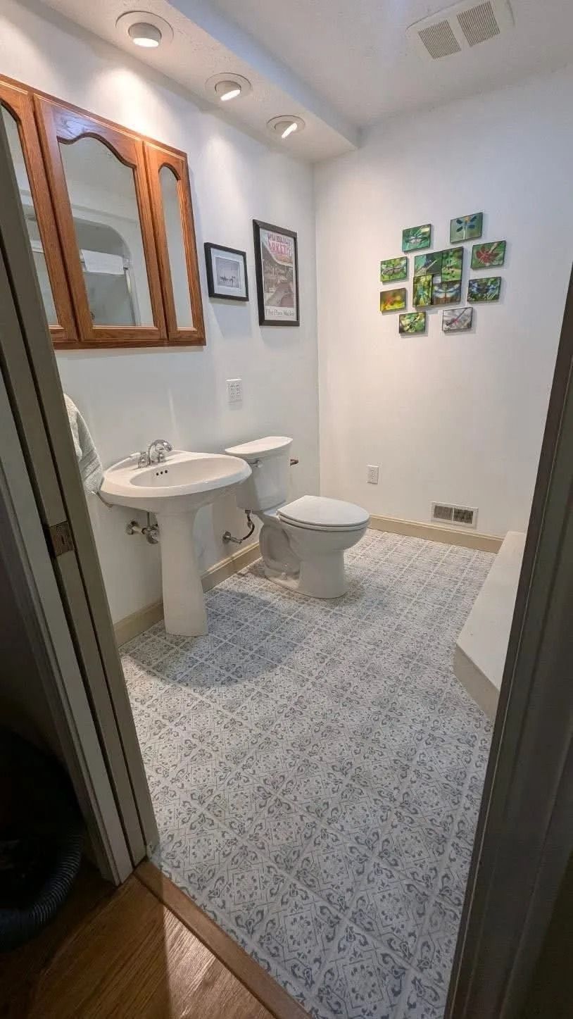Small white bathroom with sink, toilet, mirror, and patterned tile floor.
