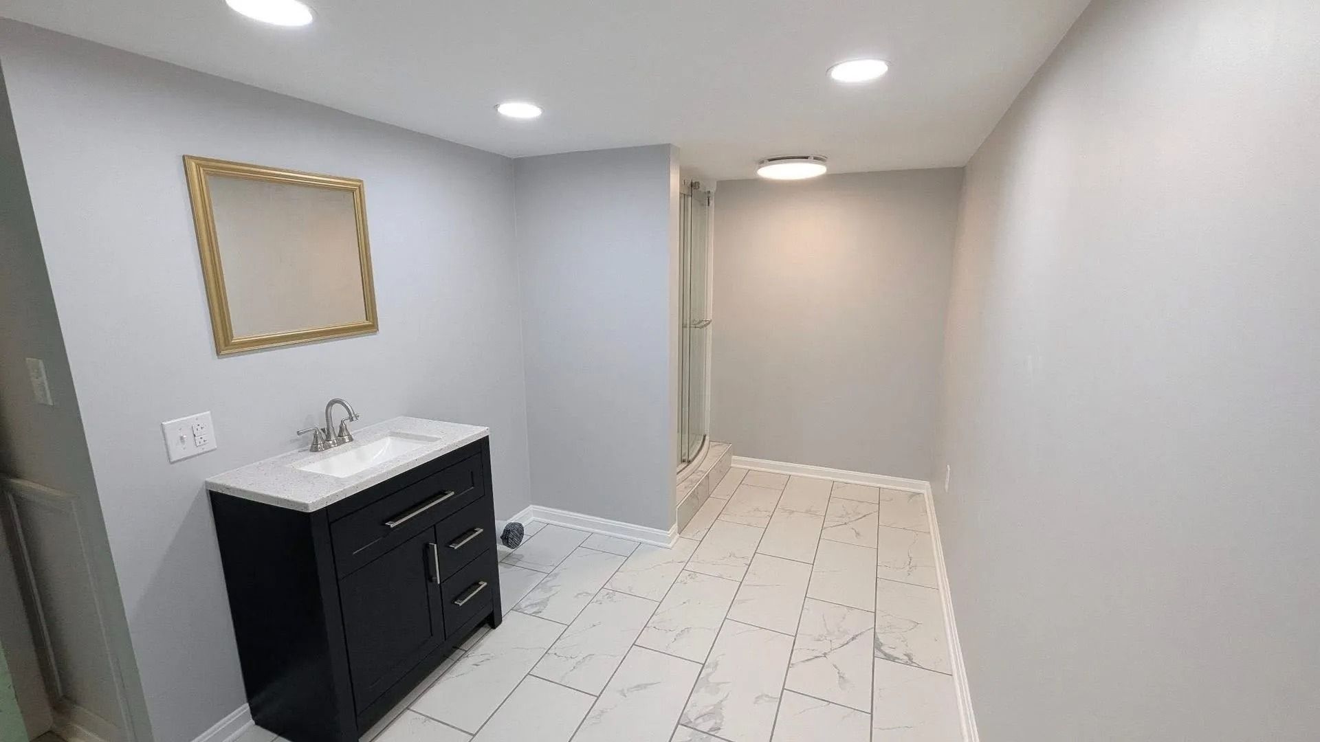 Small bathroom with black vanity, gold-framed mirror, and light gray tile floor.