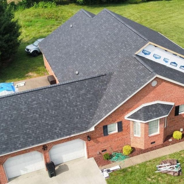 Aerial view of a brick house with gray shingle roof, double garage, and a car parked beside it.
