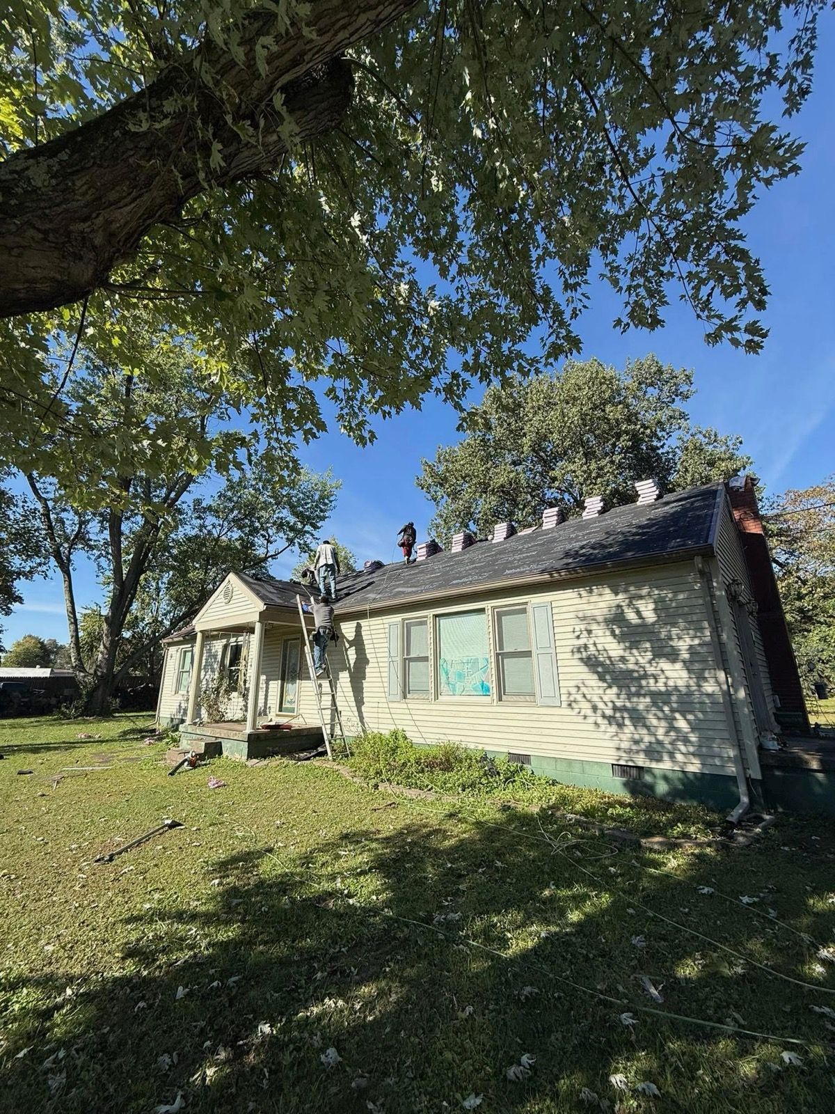Small white house with a porch under large trees on a sunny day