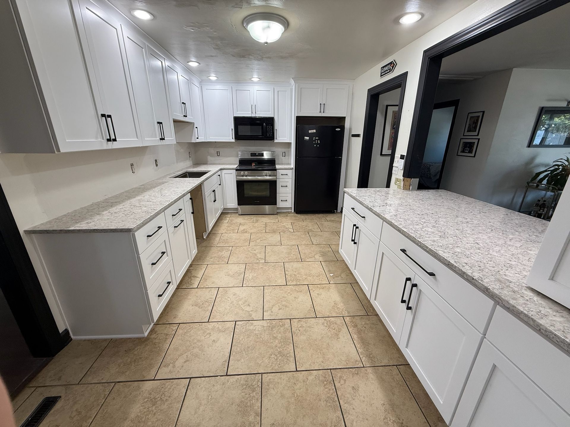 Bright white kitchen with granite counters, beige tile floor, black appliances, and a large pass-through window.
