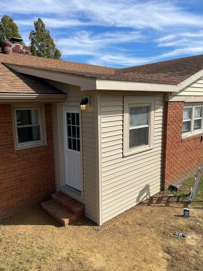 Small beige side entry with white door and window, attached to red brick house under a shingled roof.