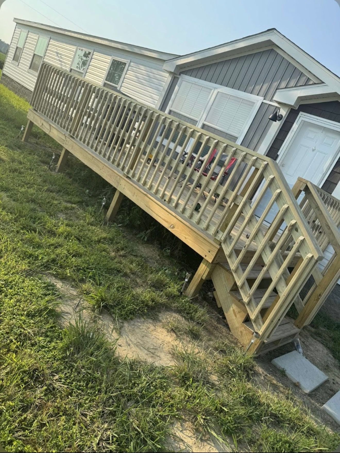 Tilting wooden ramp leading to a mobile home on a grassy lot