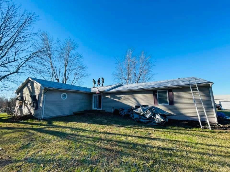 Collapsed gray house with damaged roof in a grassy yard under a clear blue sky