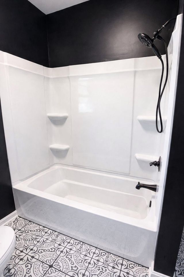 Modern black-and-white bathroom with a white bathtub, showerhead, and patterned tile floor.