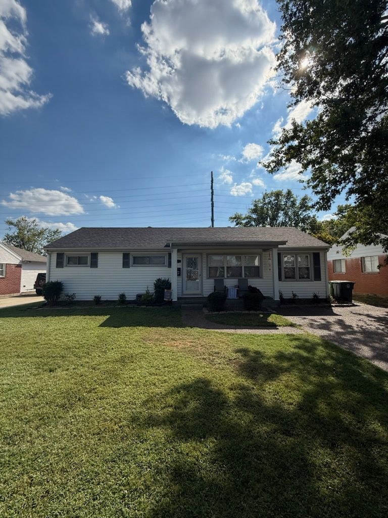 Single-story white house with a front porch and large grassy yard under a partly cloudy sky.