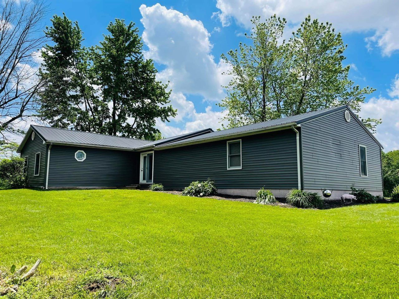 Dark gray house with white trim on a bright green lawn under a partly cloudy sky