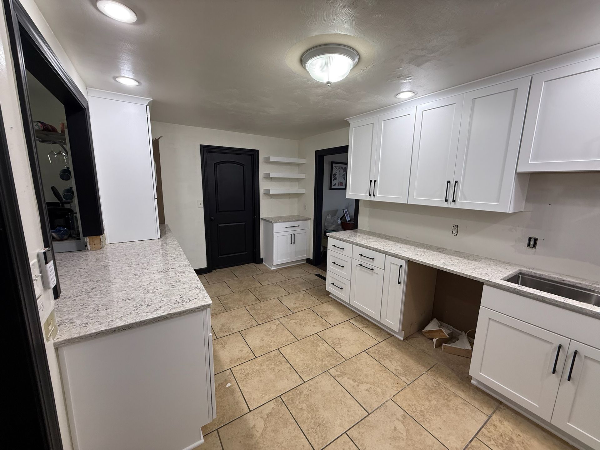 Empty kitchen with white cabinets, tiled floor, black door, and granite countertops.