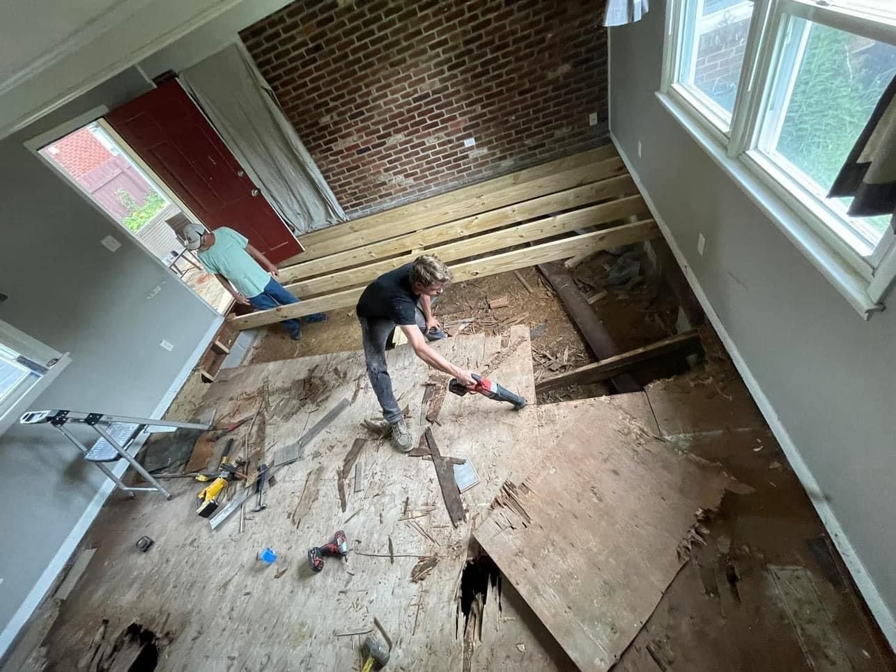 Person removing floorboards in a room with exposed subfloor and brick walls