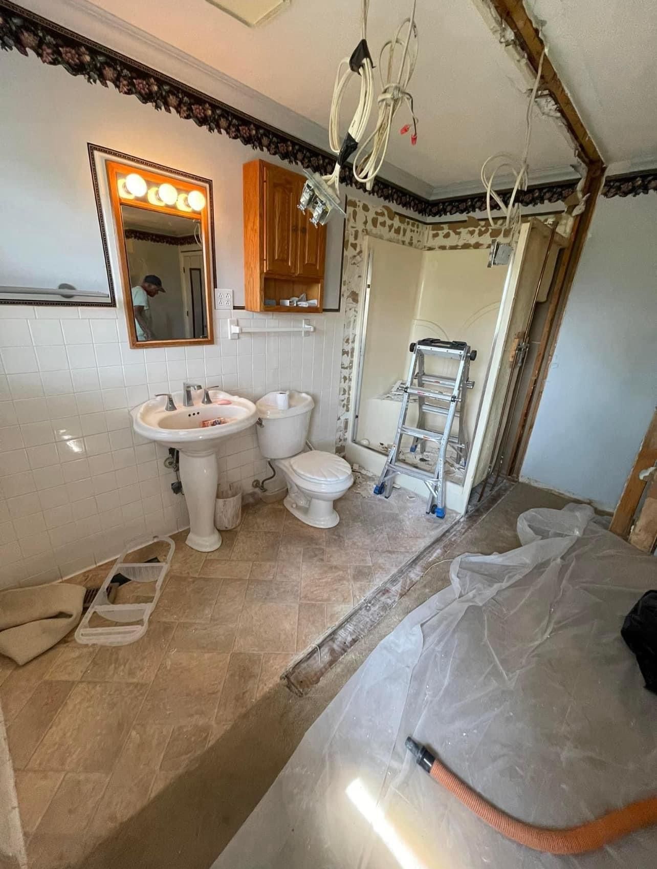 Partially renovated bathroom with sink, toilet, ladder, and plastic-covered floor under construction