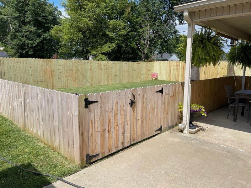 Wooden fenced backyard corner beside a concrete patio and covered carport.