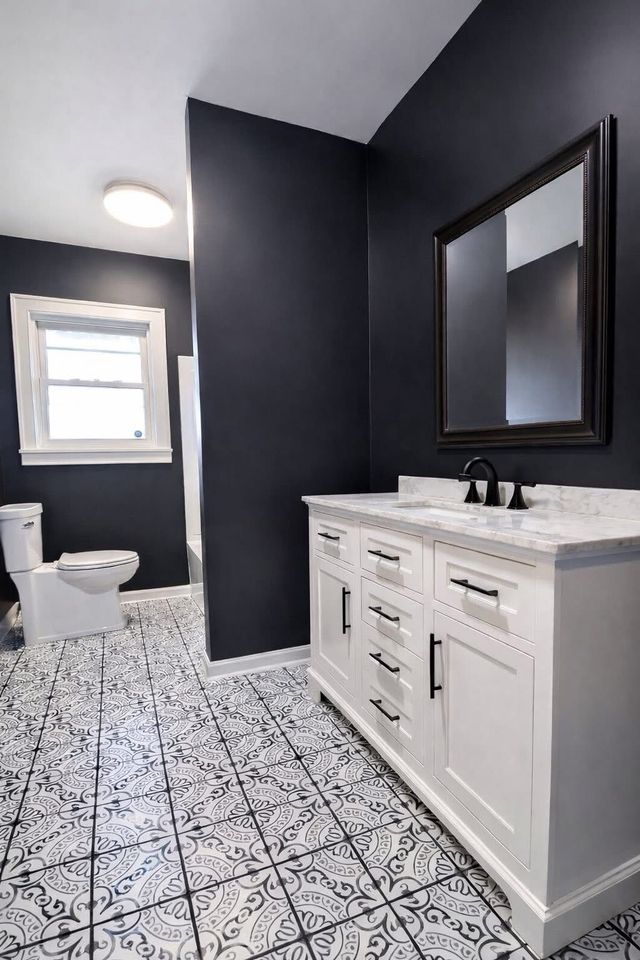 Modern bathroom with black walls, white vanity, patterned tile floor, and toilet near a window