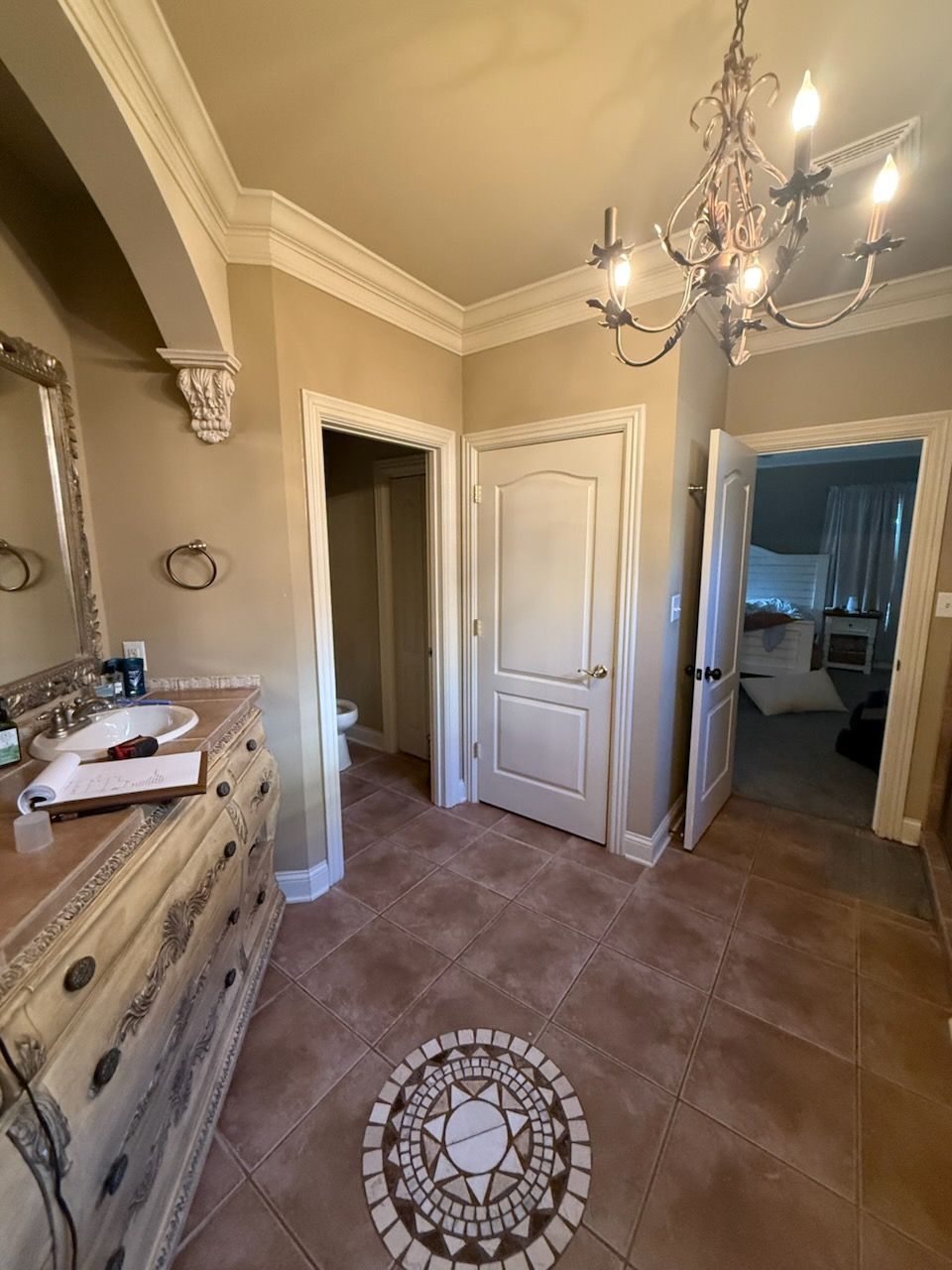 Elegant beige hallway with chandelier, decorative dresser, and open doorway to a bedroom