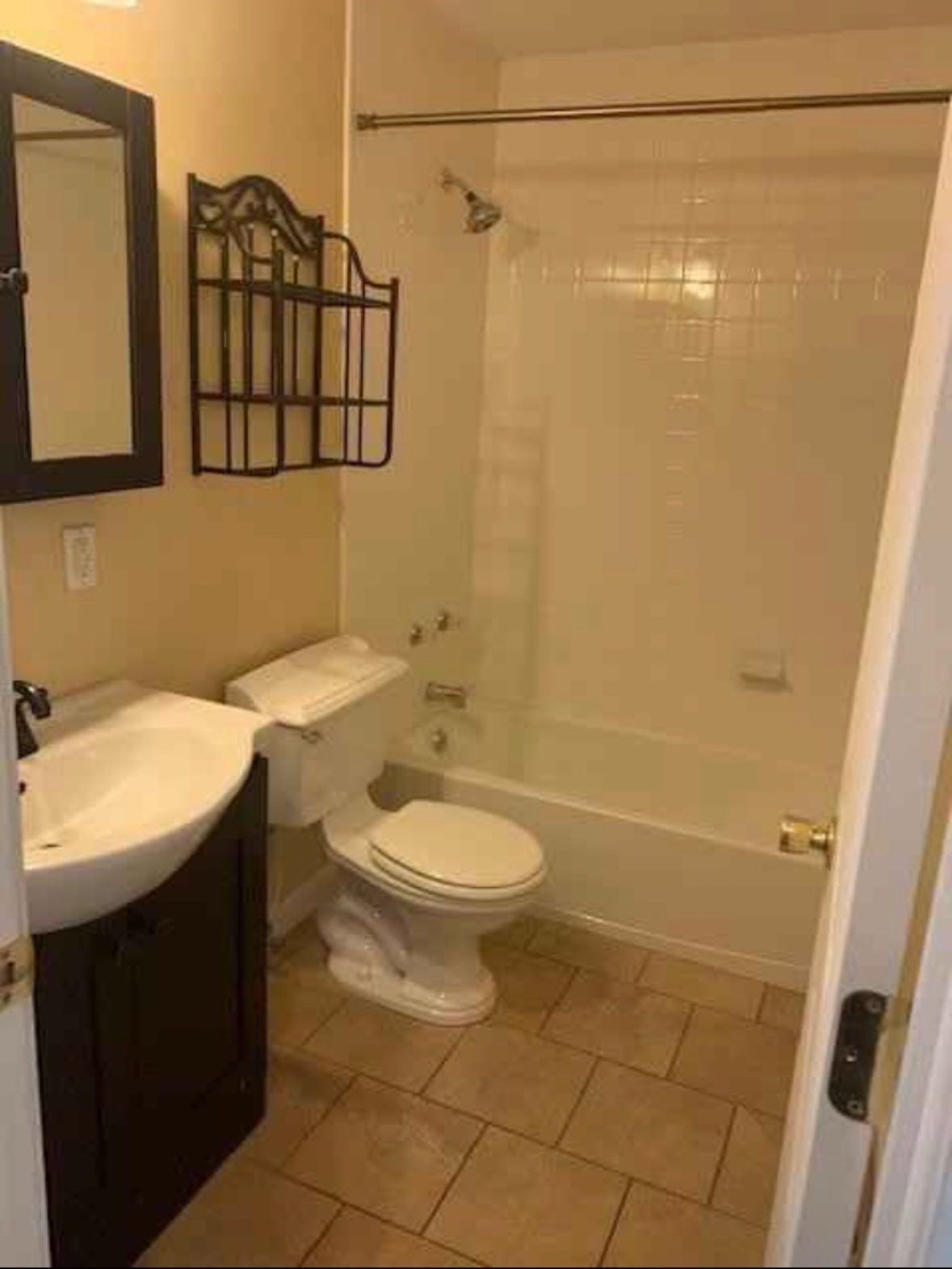 Small beige bathroom with sink, toilet, tub-shower, tan tile floor, and wall mirror.