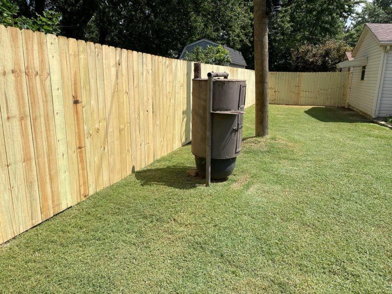 Backyard with wooden privacy fence, grassy lawn, and a trash bin by a tree support pole