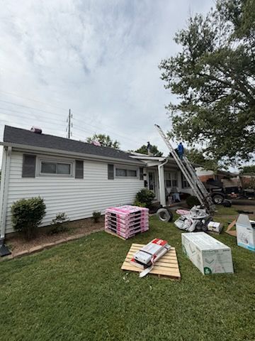 Single-story house yard with stacked construction materials and debris near a ladder by the side wall