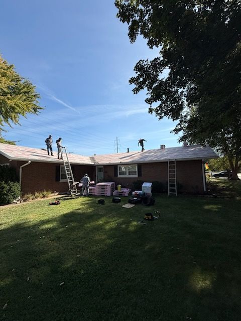 People on a roof repairing shingles, with ladders and patio chairs in a sunny backyard
