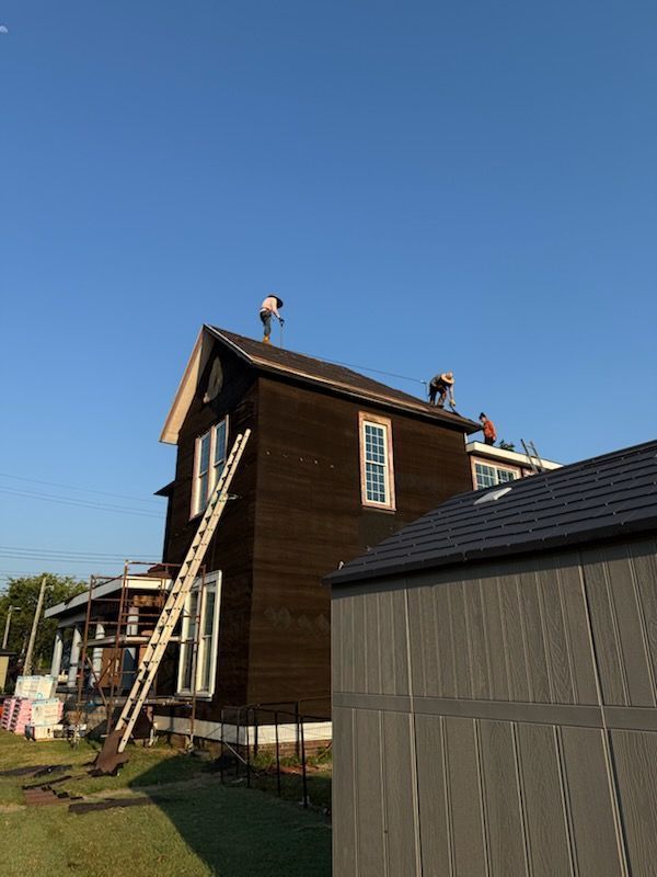 Two-story house under construction with workers on the roof and scaffolding beside it