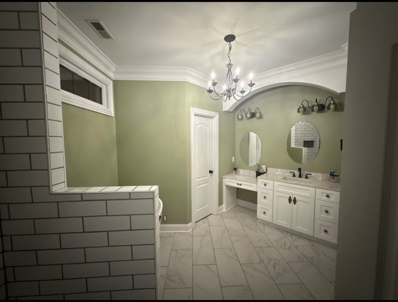 Elegant bathroom with white vanity, oval mirrors, green walls, and tiled floor under a chandelier