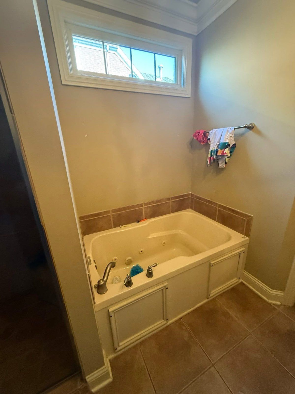 Bathroom with corner soaking tub, tan tile floor, and small window above.
