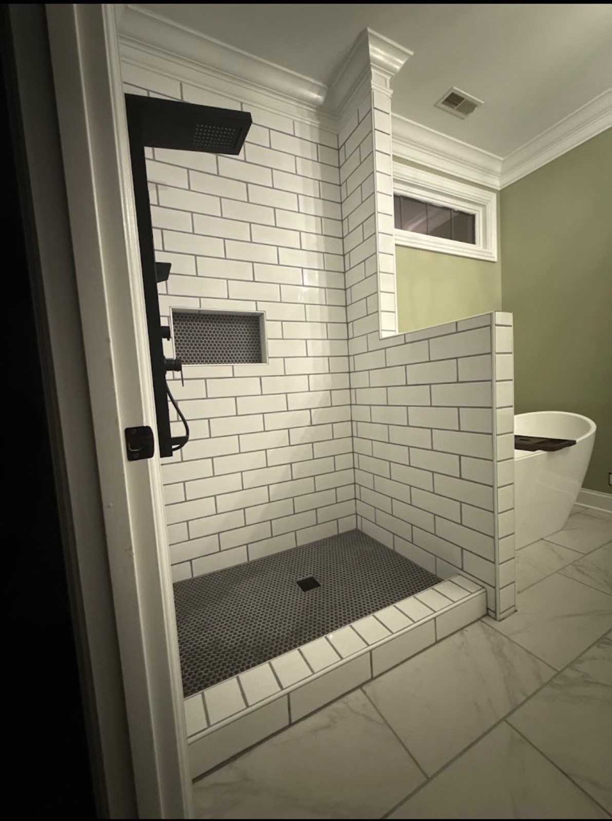 Walk-in shower with white subway tile, black fixtures, and a glass partition in a bathroom.