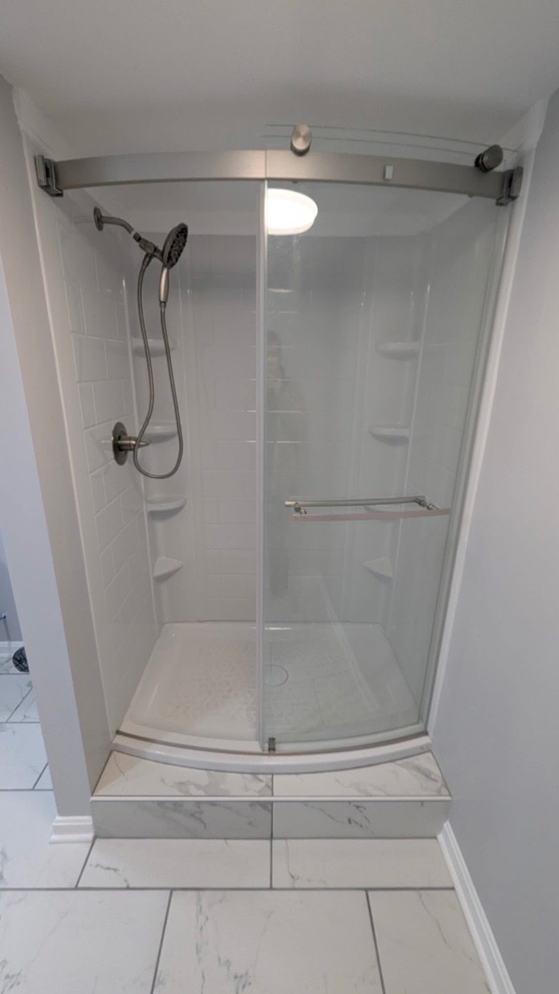 Clear glass shower enclosure with chrome frame and handheld showerhead in a white bathroom.