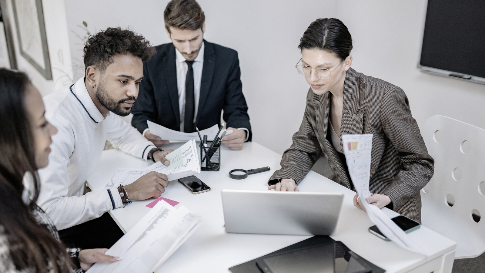 People in a glass-walled meeting room collaborating around laptops and documents