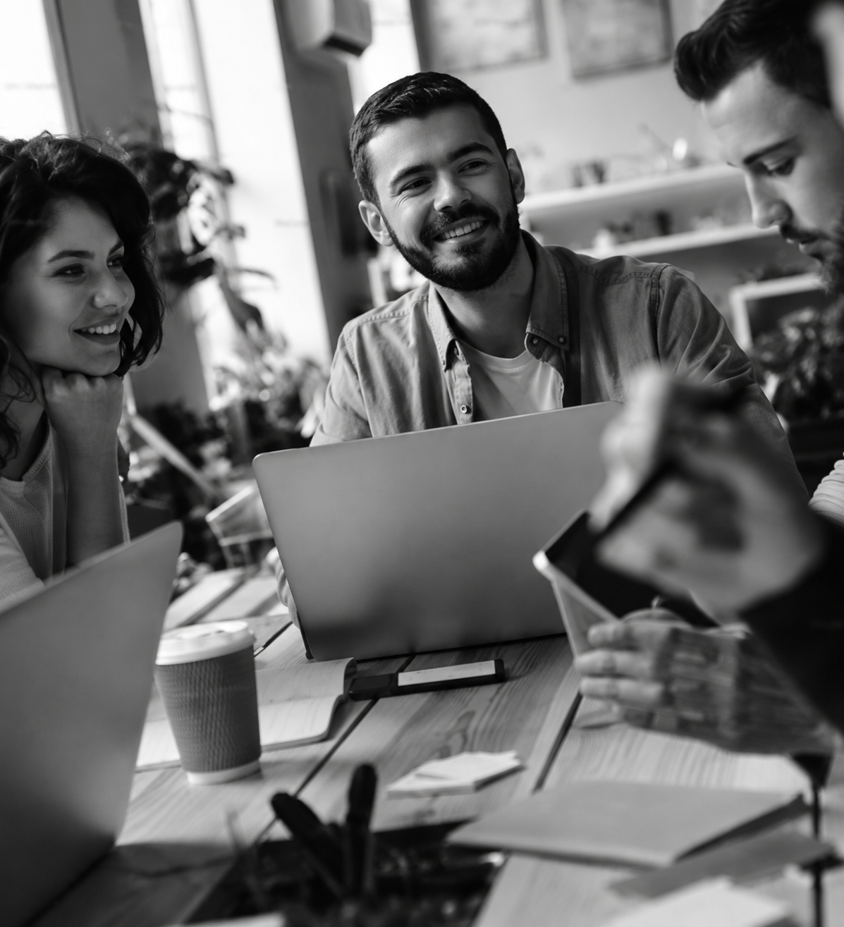 People collaborating around laptops at a table in a bright office, smiling and discussing work.