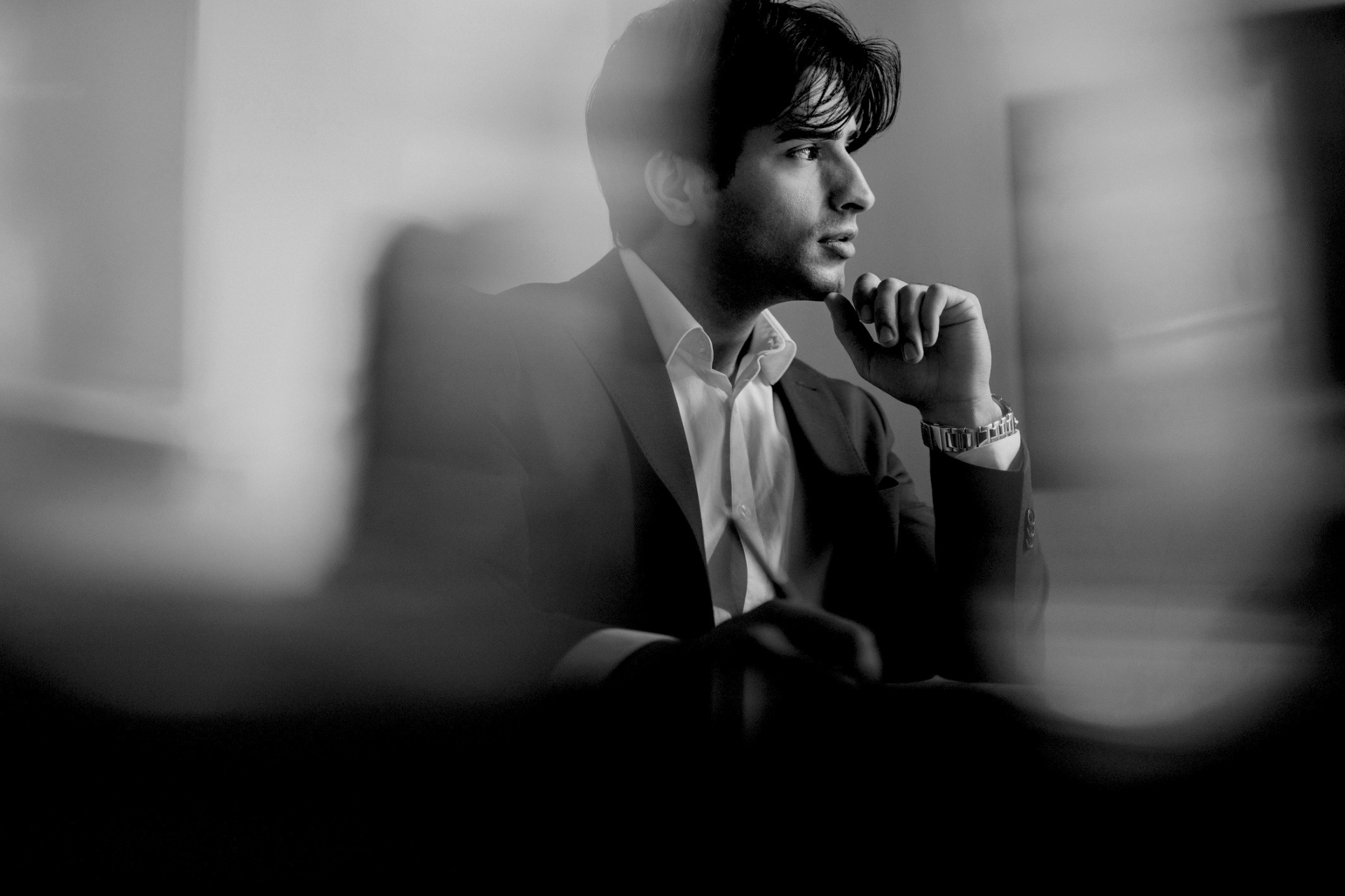 Black-and-white portrait of a thoughtful man in a suit, seated with his hand on his chin.