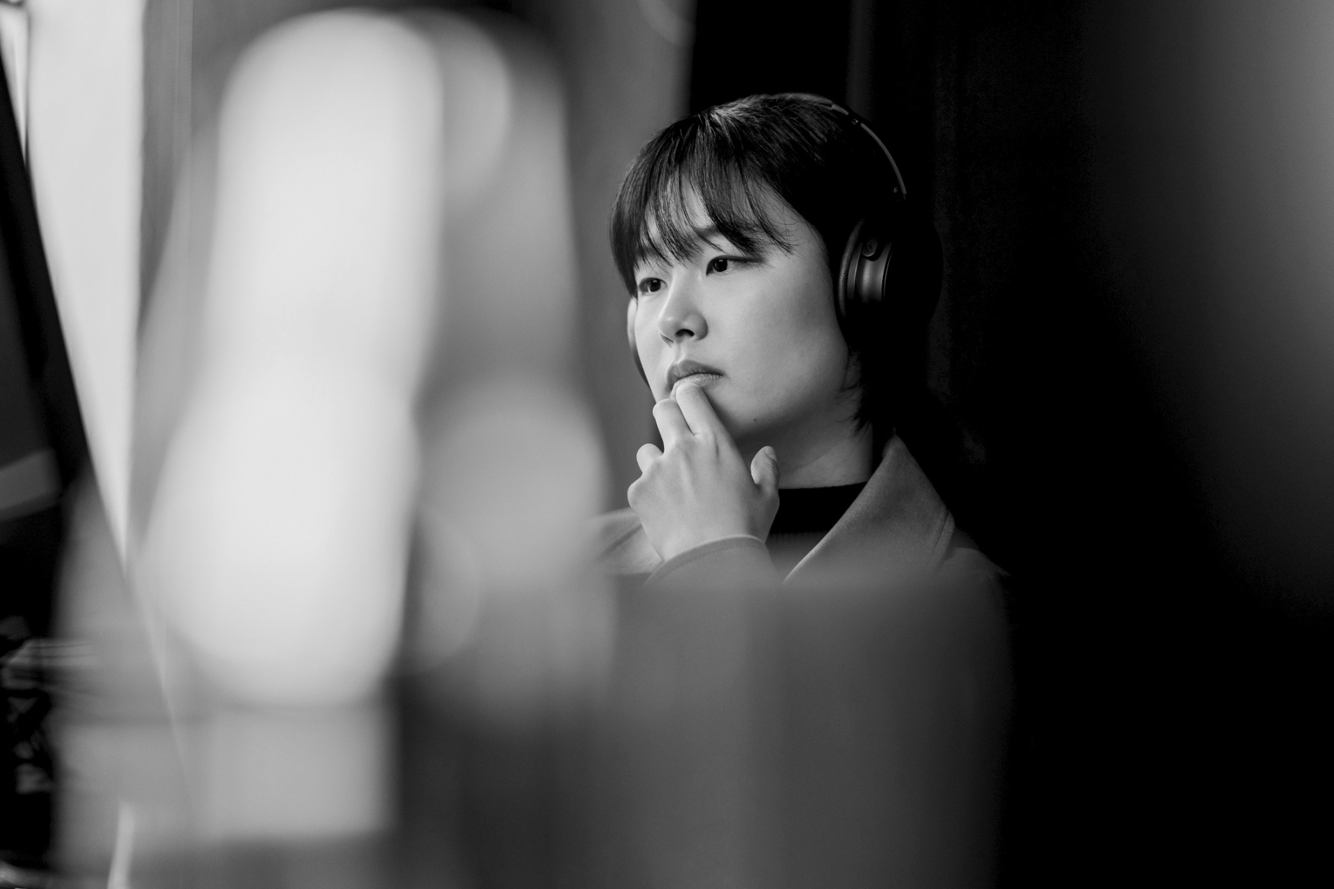 Woman wearing headphones and touching her lips, seen in a black-and-white studio scene