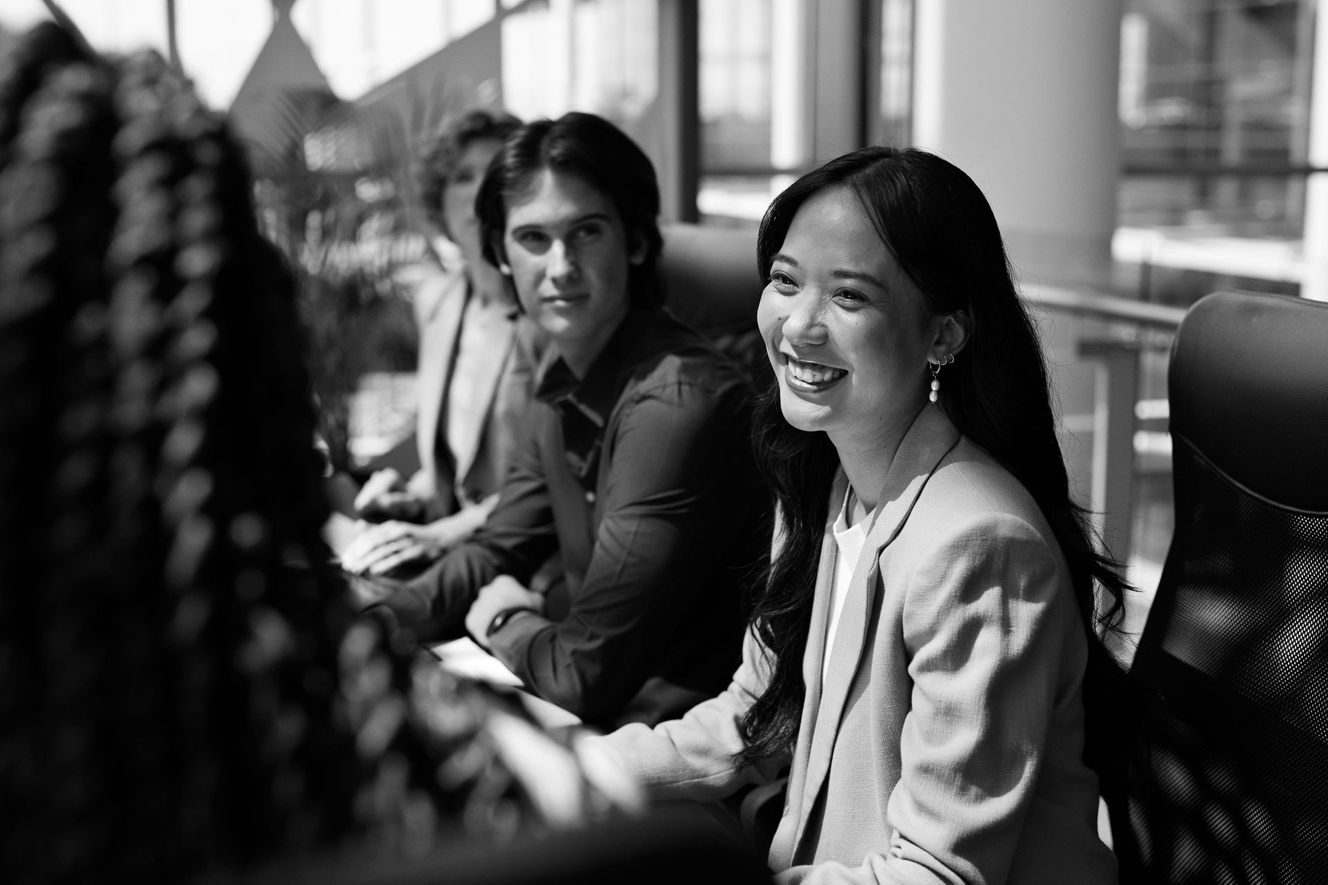 People seated in a bright office meeting, one woman smiling toward the camera.