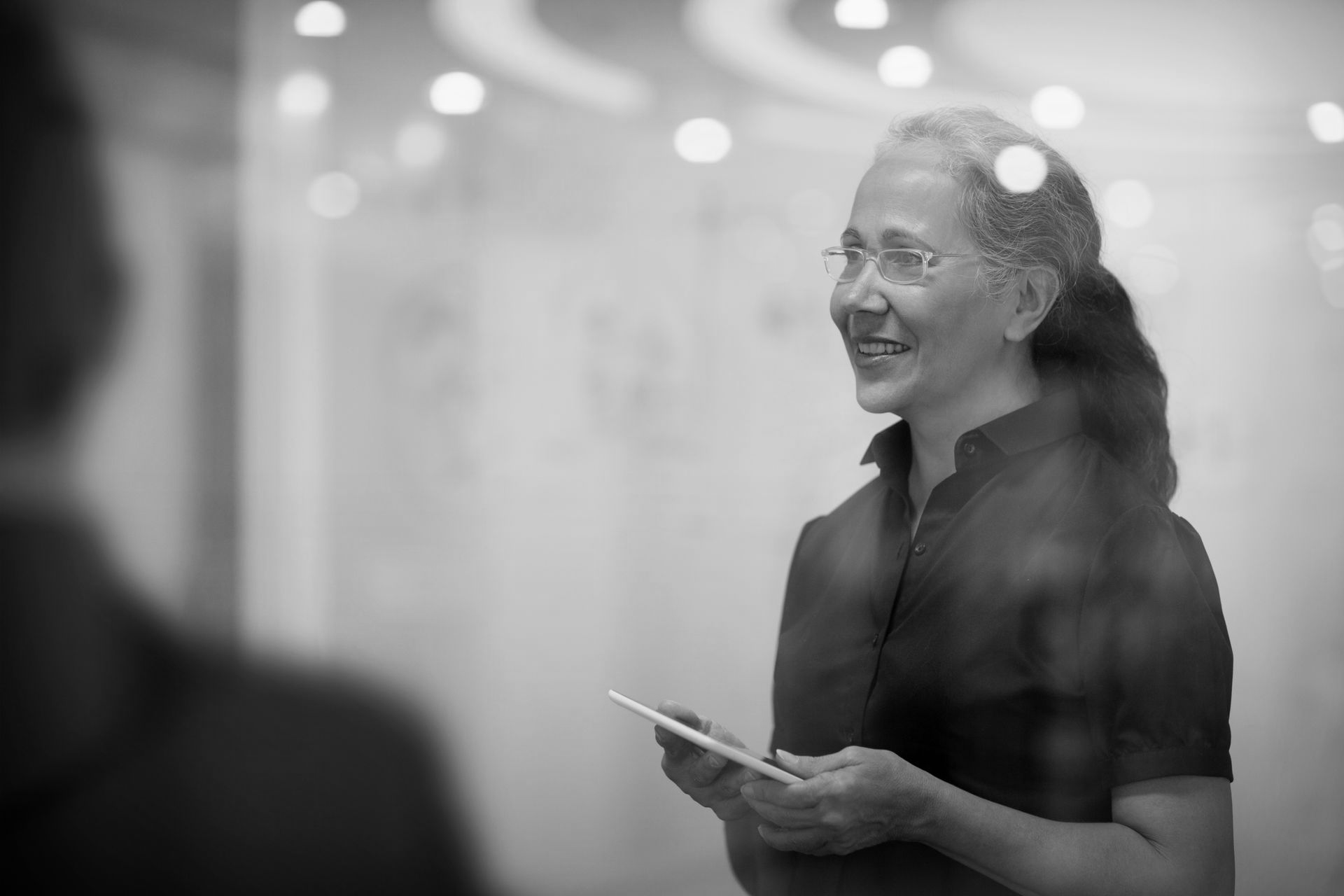 Colleagues talking in an office, with one woman standing by a computer monitor and sticky notes on the wall.