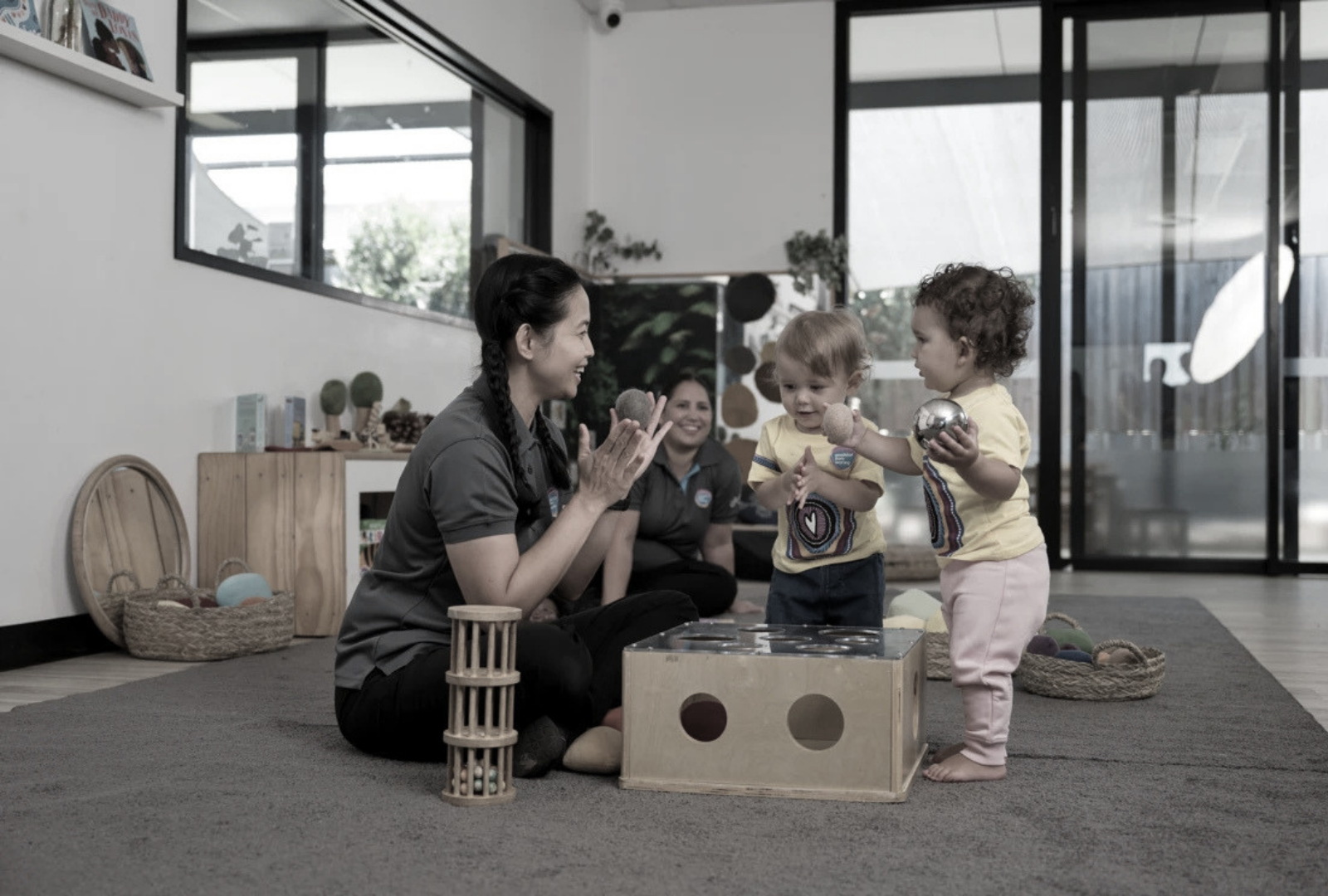 Adult and three children play with toys on a rug in a bright indoor living room
