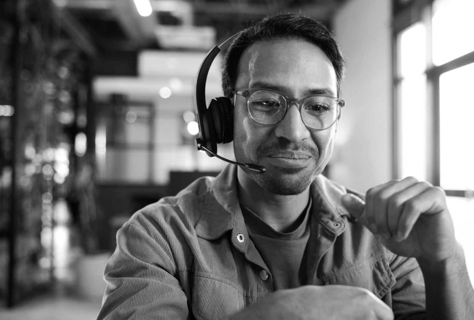 Smiling man wearing a headset in a modern office, seated at a desk and looking at a laptop