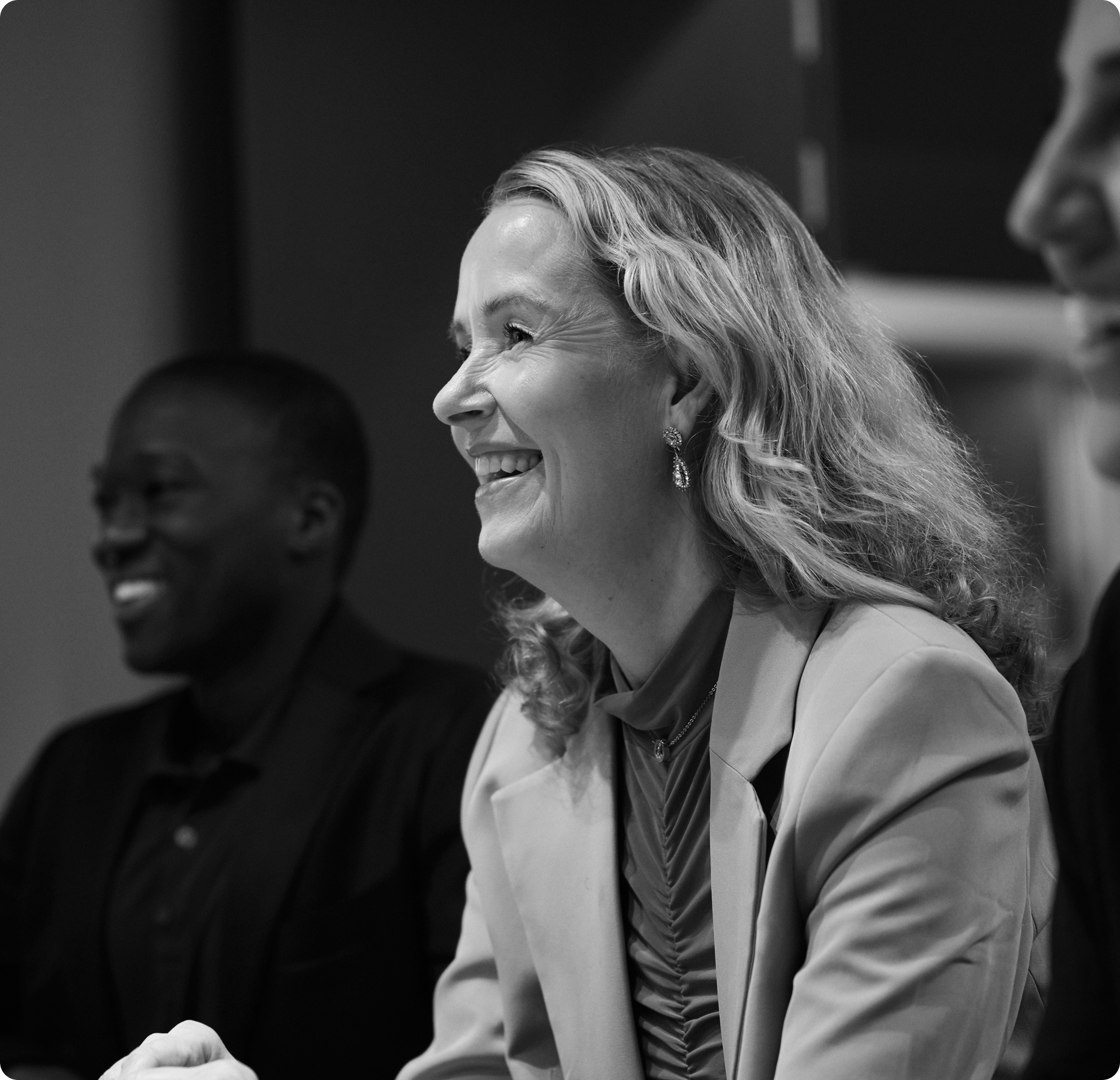 Two people smiling and laughing at a formal event, with a woman in a blazer in the foreground.