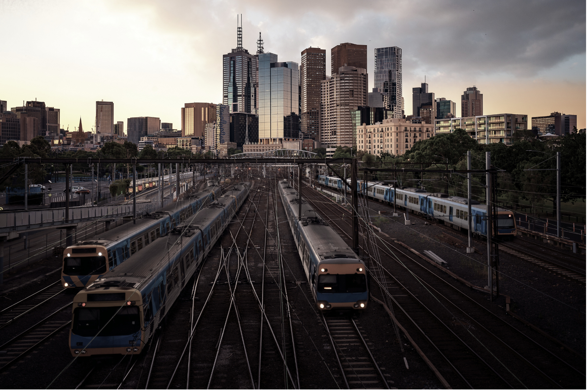 Trains on multiple tracks beneath a city skyline at dusk