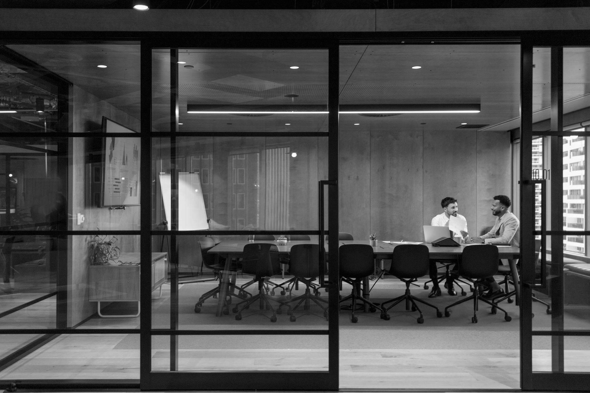 People meeting in a modern glass-walled conference room, viewed through the office entrance.
