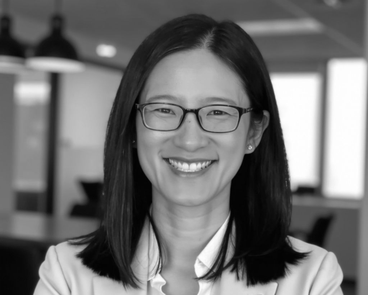Smiling person with glasses in a blurred office setting.