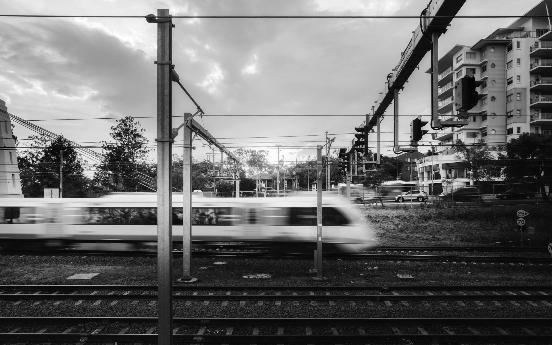 Blurry white train speeding past railway tracks in a black-and-white urban scene with apartment buildings.