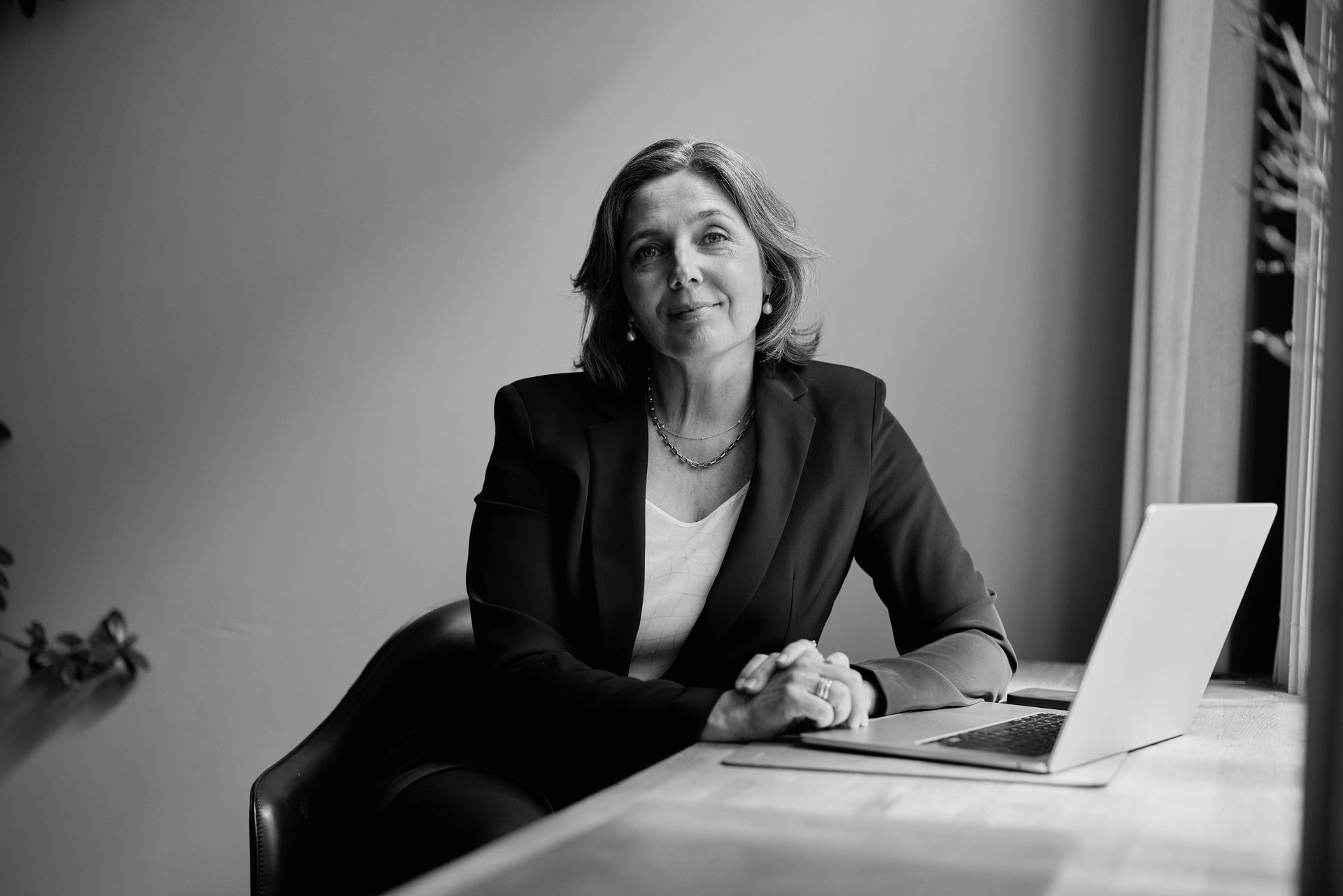 Person seated at a table with a laptop, smiling in a black-and-white office setting.