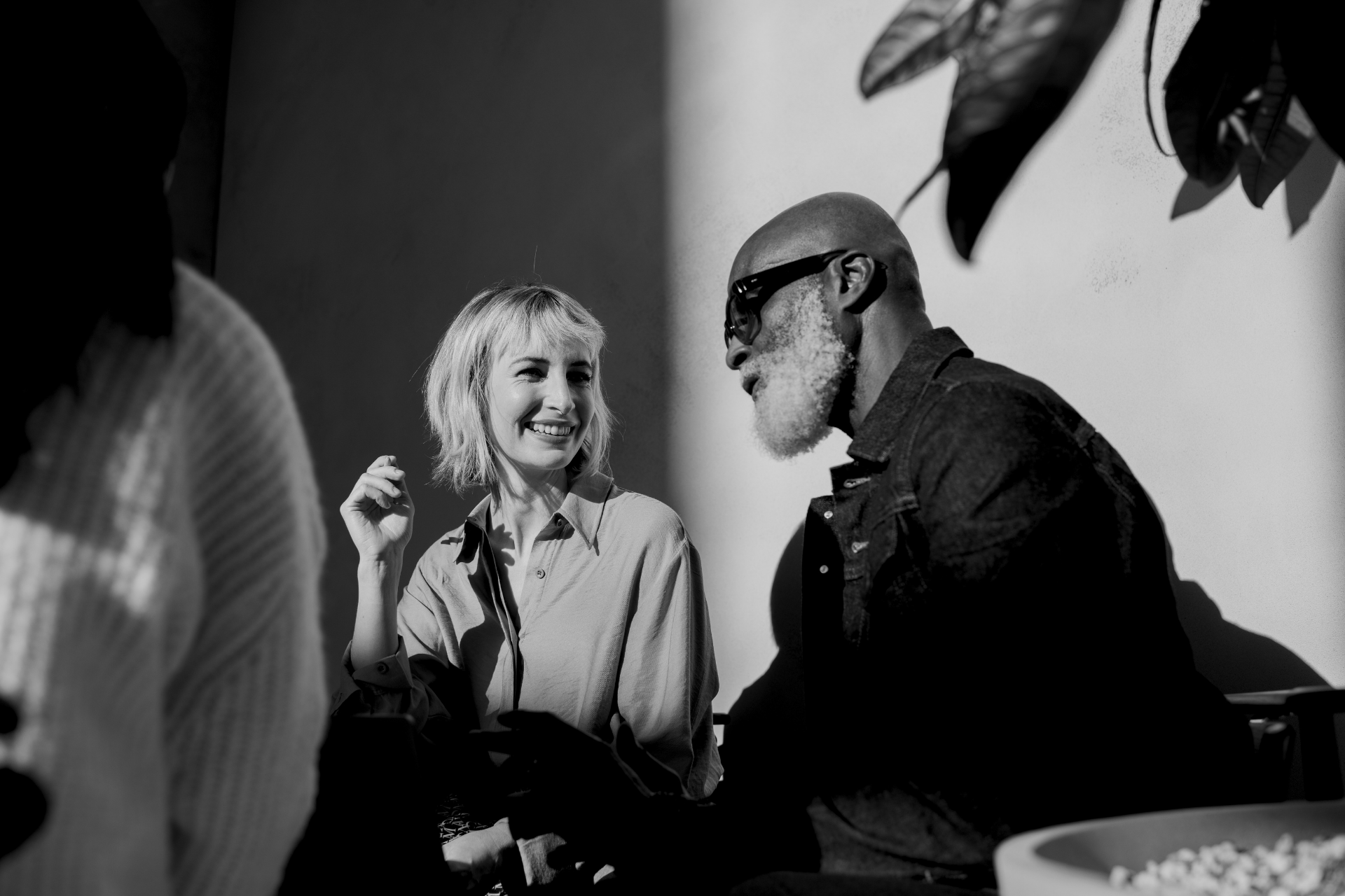 Two people talking at a table in a black-and-white photo, one smiling and holding a drink