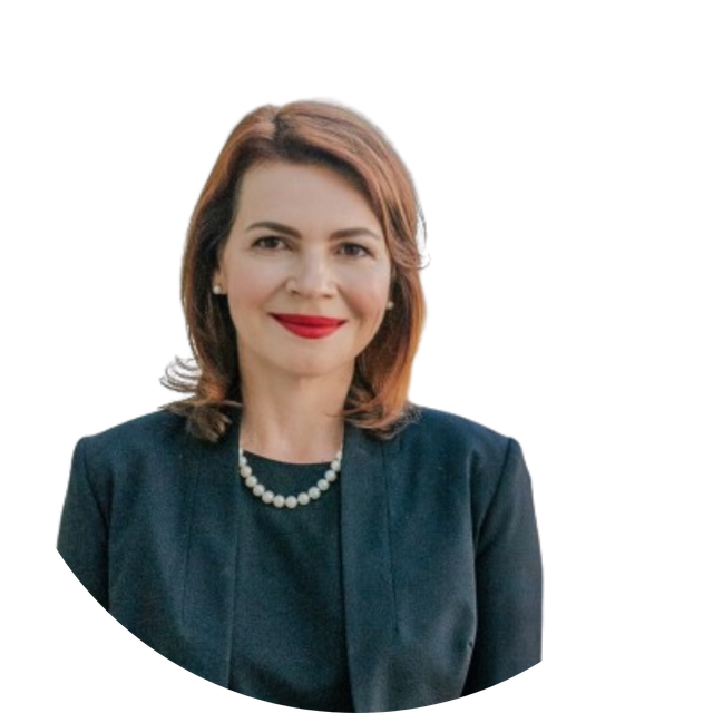 Smiling professional in a blazer standing in a modern office with blurred desks and windows behind her