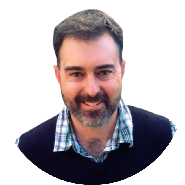 Smiling man with short dark hair and beard, wearing a checkered shirt and dark sweater on a white background